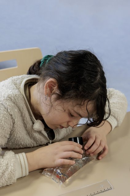Une petite fille observe au microscope un organisme vivant lors d'un atelier des petits recollets
